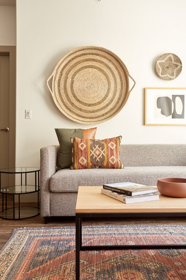 Southwestern living room with taupe couch, wood and metal coffee table, baskets on wall, art, pillows.